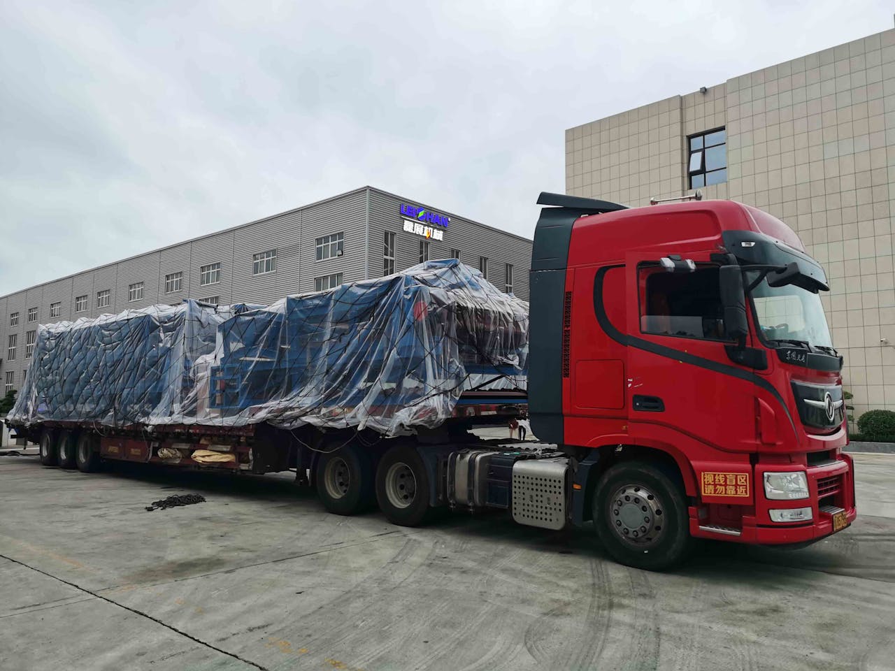 creative-03 Red truck with large covered cargo in an industrial area, overcast day.