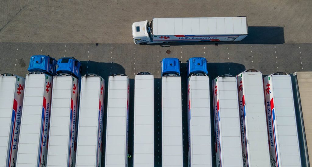 pexels photo 13961751 1 Top-down drone shot of logistics trucks arranged in a row in a parking lot.